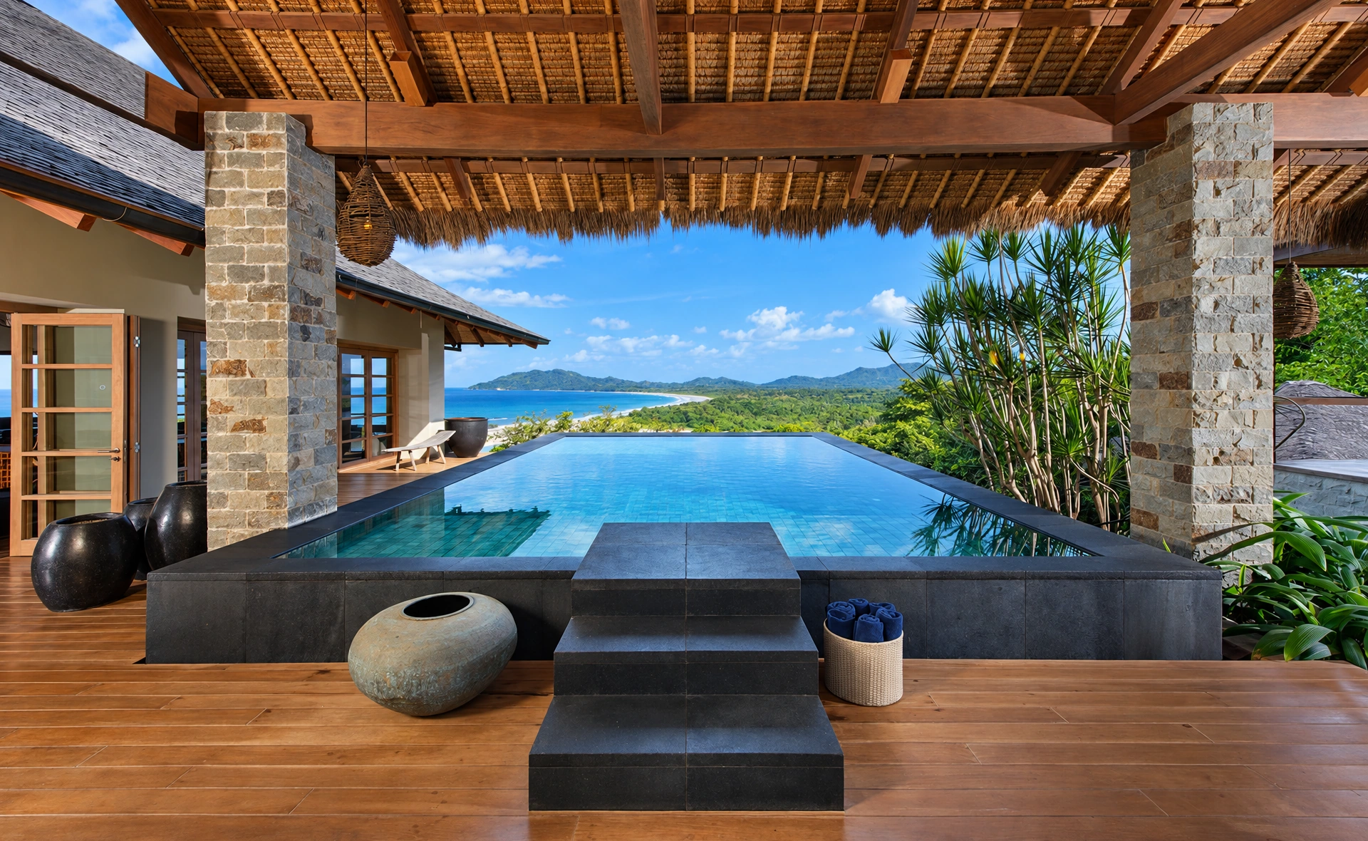 A stone-framed infinity pool and coastal view at Tamarindo 8BR Balinese Villa