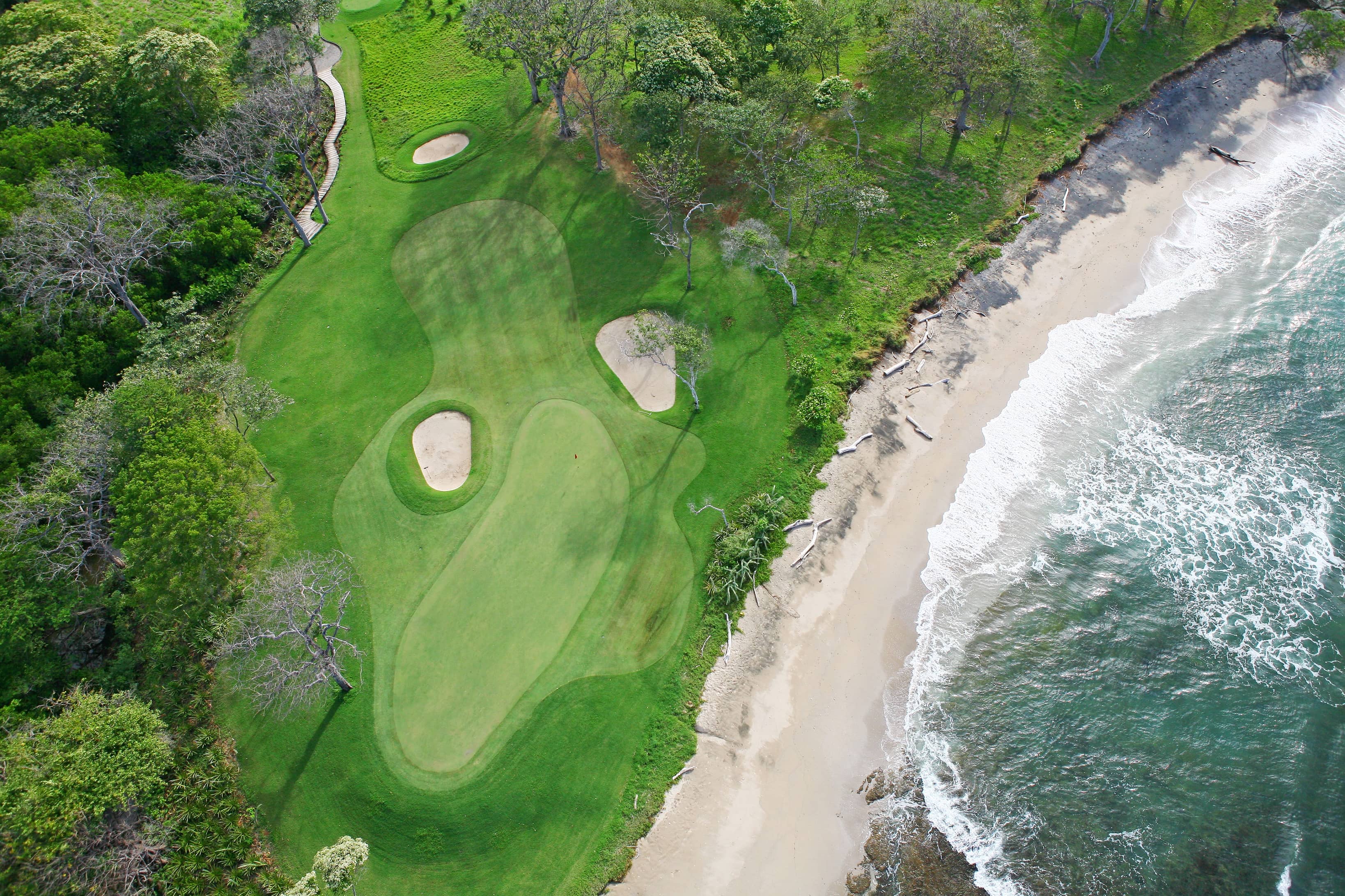 An aerial view of Hacienda Pinilla’s green fairway, sandy beach and Pacific surf